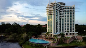 Un hotel de gran altura con piscina, rodeado de vegetación y un río.