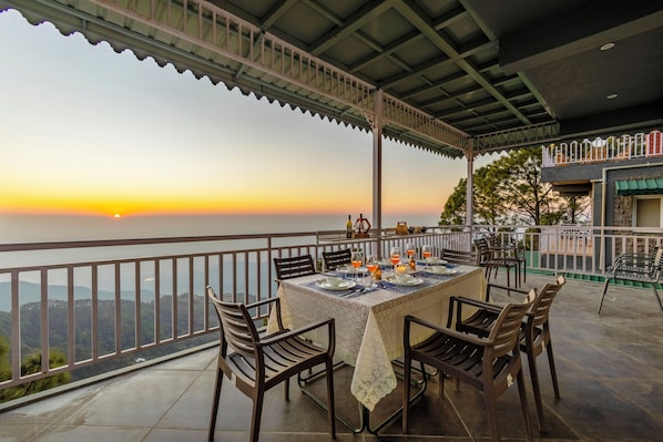 A terrace with a table set for dining, chairs, and a railing overlooking a scenic view. - ELIVAAS Alpenglow 3 BHK Villa (Kasauli)