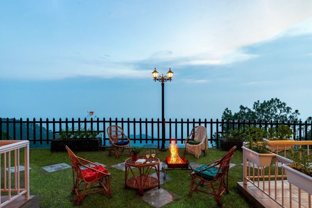 Un patio con sillas de mimbre, una mesita, una chimenea y un farol.