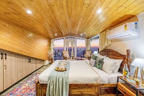 A wooden-paneled room with a bed, a small table, and a view of the sunset. - ELIVAAS Alpenglow 3 BHK Villa (Kasauli)