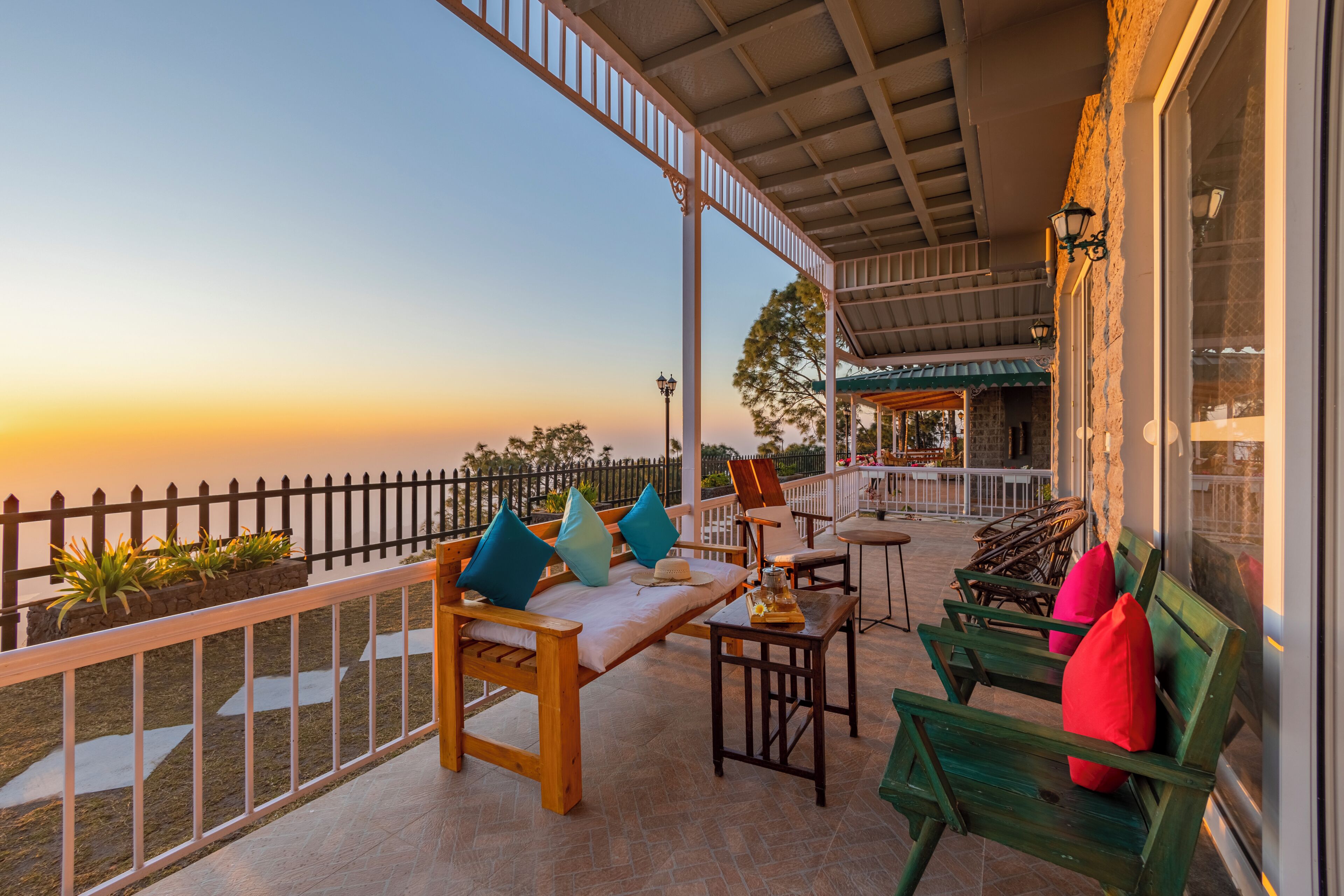 Una terraza con mobiliario exterior, barandilla y vista al atardecer.