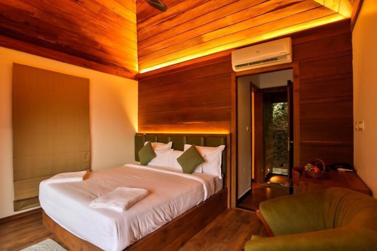Een slaapkamer met een houten plafond, een bed met wit beddengoed, een groene stoel en een airconditioning.