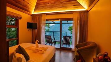 A hotel room with a bed, a television, a balcony with chairs, and a view of the outdoors.