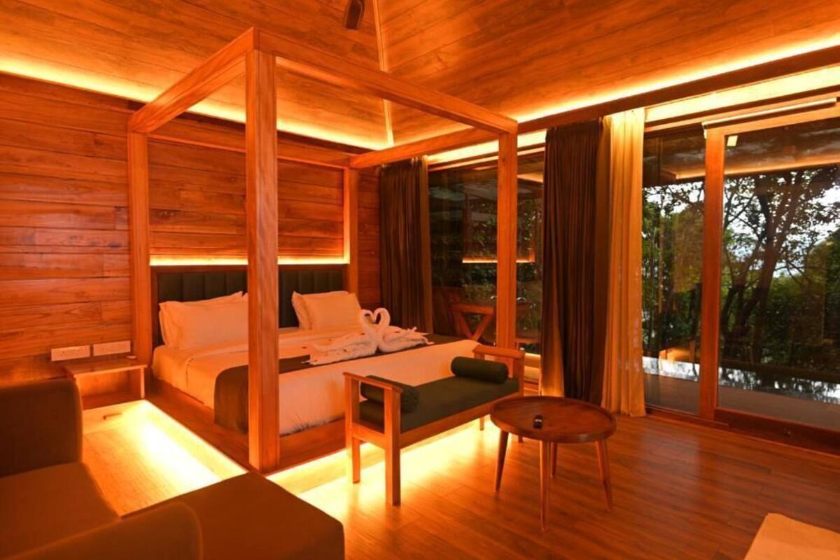 Een bed met houten slaaphemel, een uitzicht op een meer, een tafeltje en een bank in een kamer met grote ramen.