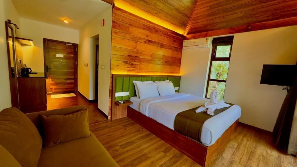 A wooden-paneled room with a bed, a sofa, a television, and a window.
