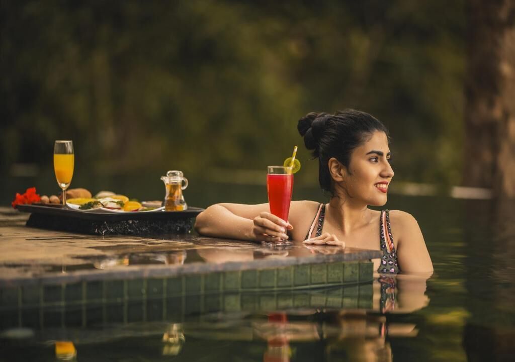 A person relaxing by a pool with a drink and a tray of food.