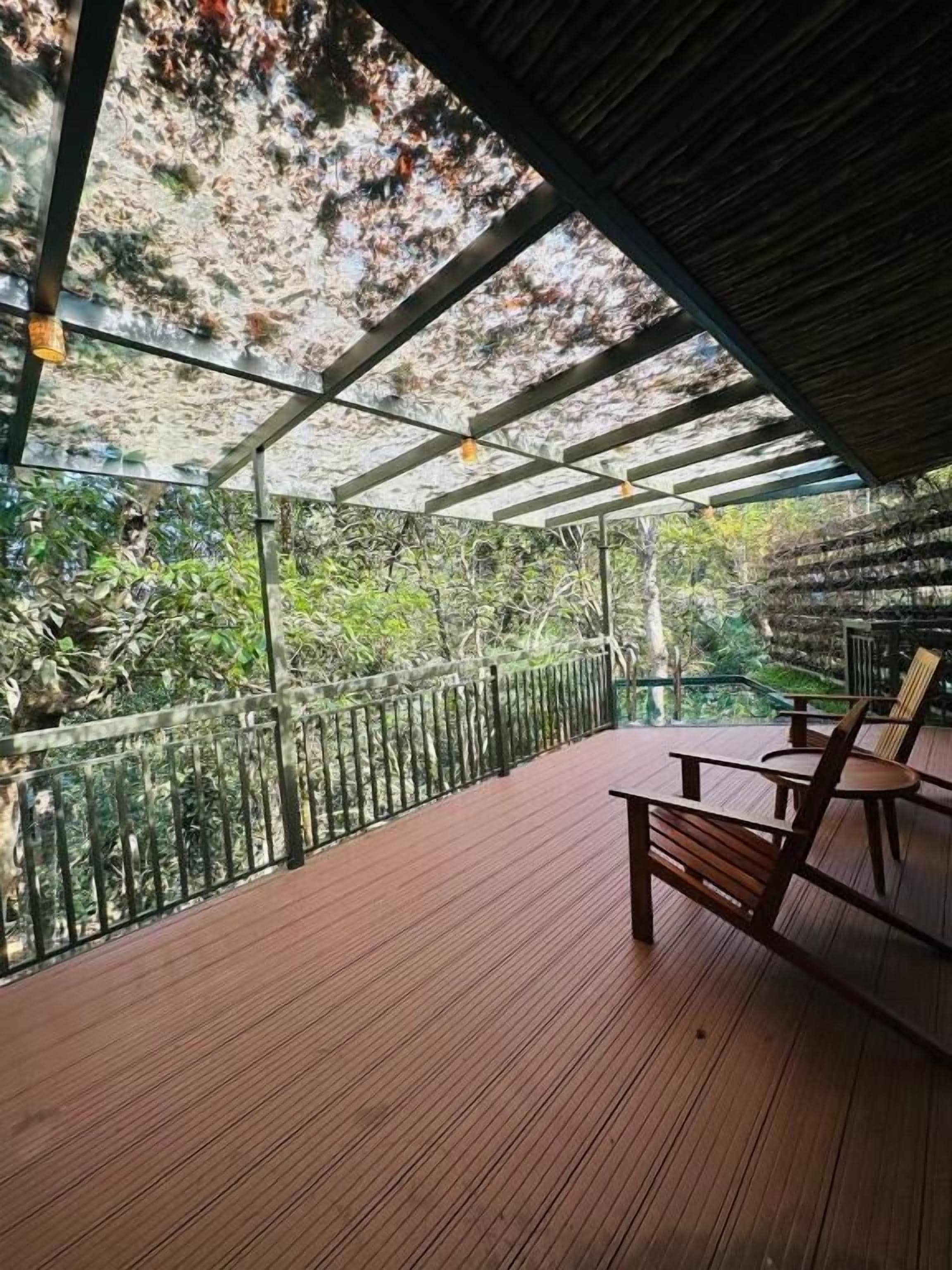 Um deck de madeira com guarda-corpo de vidro, com vista para um jardim.