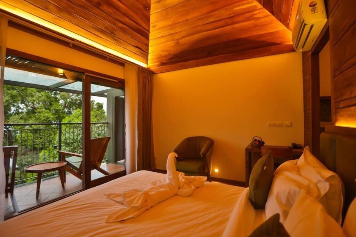 Hotelkamer met een bed, een stoel, een tafel en een balkon met uitzicht op bomen.