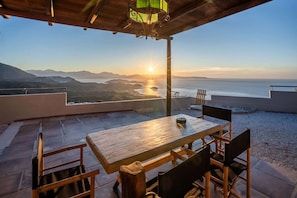 Une table et des chaises en bois sur une terrasse offrant une vue sur la mer et les montagnes.