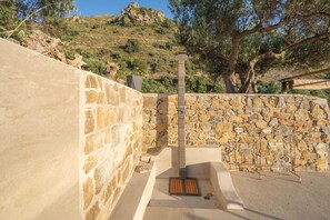 A stone wall with a metal structure, possibly a water feature, and a tree in the background.