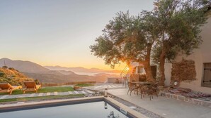 Una piscina con sillones de descanso, una mesa y vistas a montañas al atardecer.