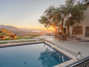 Ein Pool mit Liegestühlen, einem Tisch und Blick auf die Berge bei Sonnenuntergang.