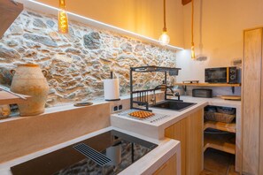 A kitchen with a stone wall, a built-in stove, a sink, and a hanging light fixture.