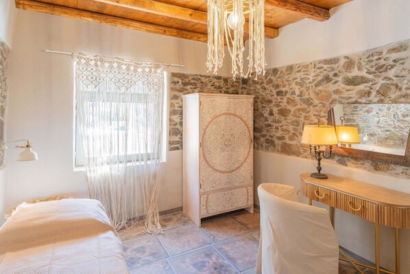 A bedroom with a bed, a wardrobe, a desk with a lamp, and a stone wall.