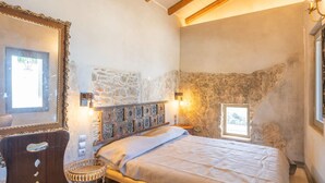 Un dormitorio con pared de piedra, una cama con cabecera estampada, una mesita y un espejo.