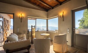 A room with a stone wall, a wooden ceiling, a large window with a view, two white chairs, and a small table. - Villa Maestoso - Private olive grove - Pool (Mirsini)
