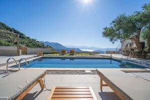 A pool area with lounge chairs, a table, and a view of mountains.