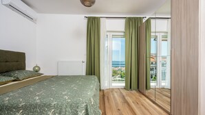 A bedroom with a bed, a radiator, a window with curtains, and a view of the outside. - Modern vacation apartment with sea view (Crikvenica)