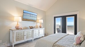 Een slaapkamer met een bed, twee bedlampen, een kaptafel, een groot raam en uitzicht op het strand.