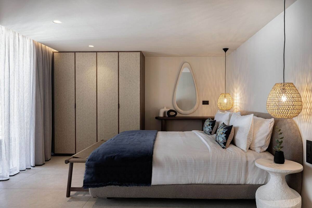 A modern bedroom with a bed, bedside table, lamp, and a large mirror.