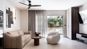 A modern living room with a sofa, armchair, coffee table, ceiling fan, and a TV on a stand. - Moncasa Suites (Agios Nikolaos)