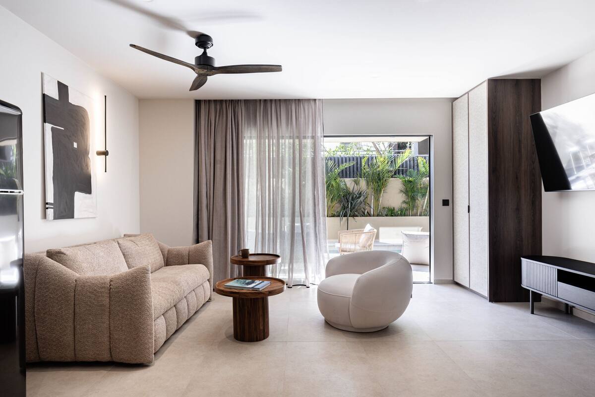 A modern living room with a sofa, armchair, coffee table, ceiling fan, and a TV on a stand.