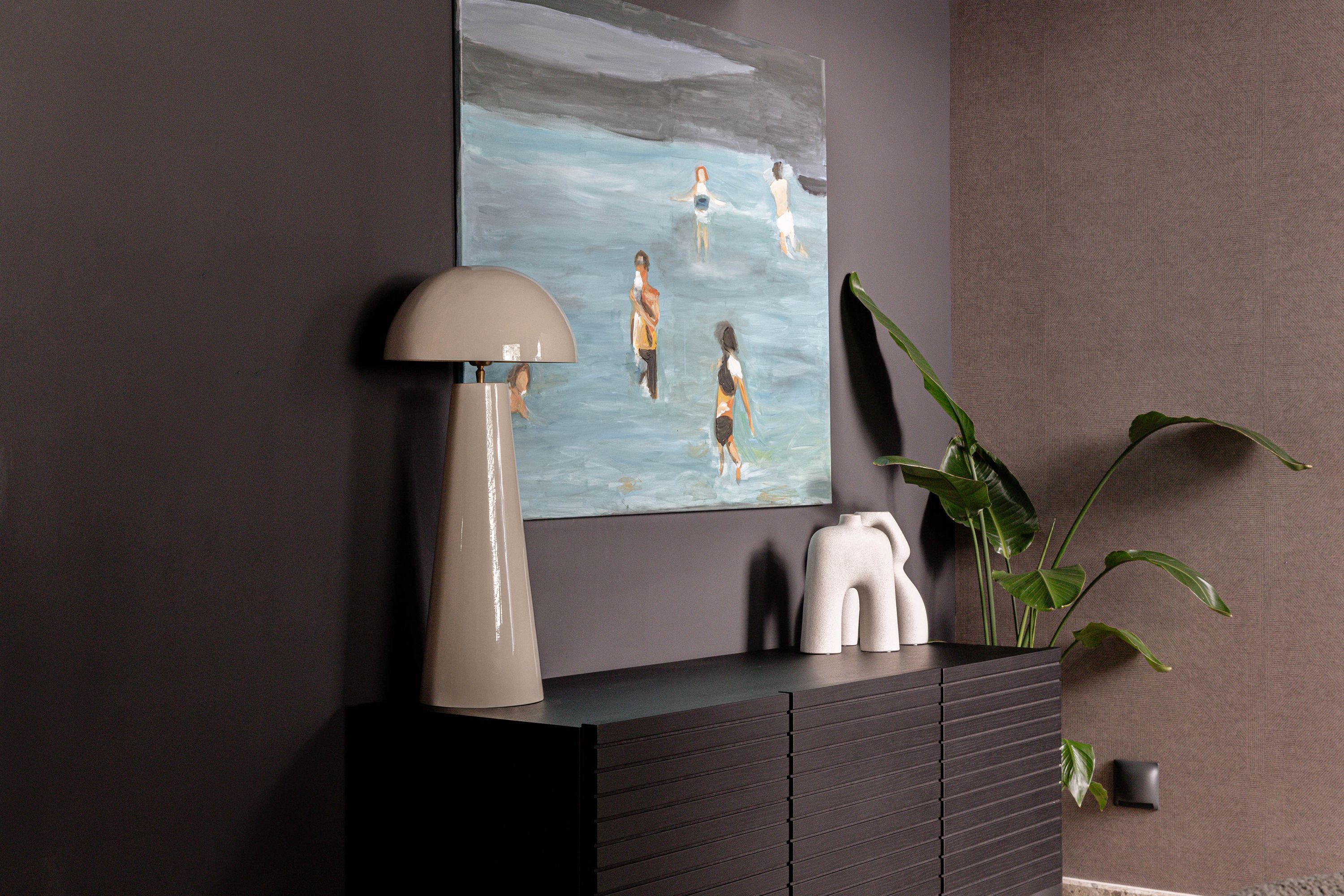 A modern interior with a painting, a lamp, and decorative items on a dark-colored cabinet.
