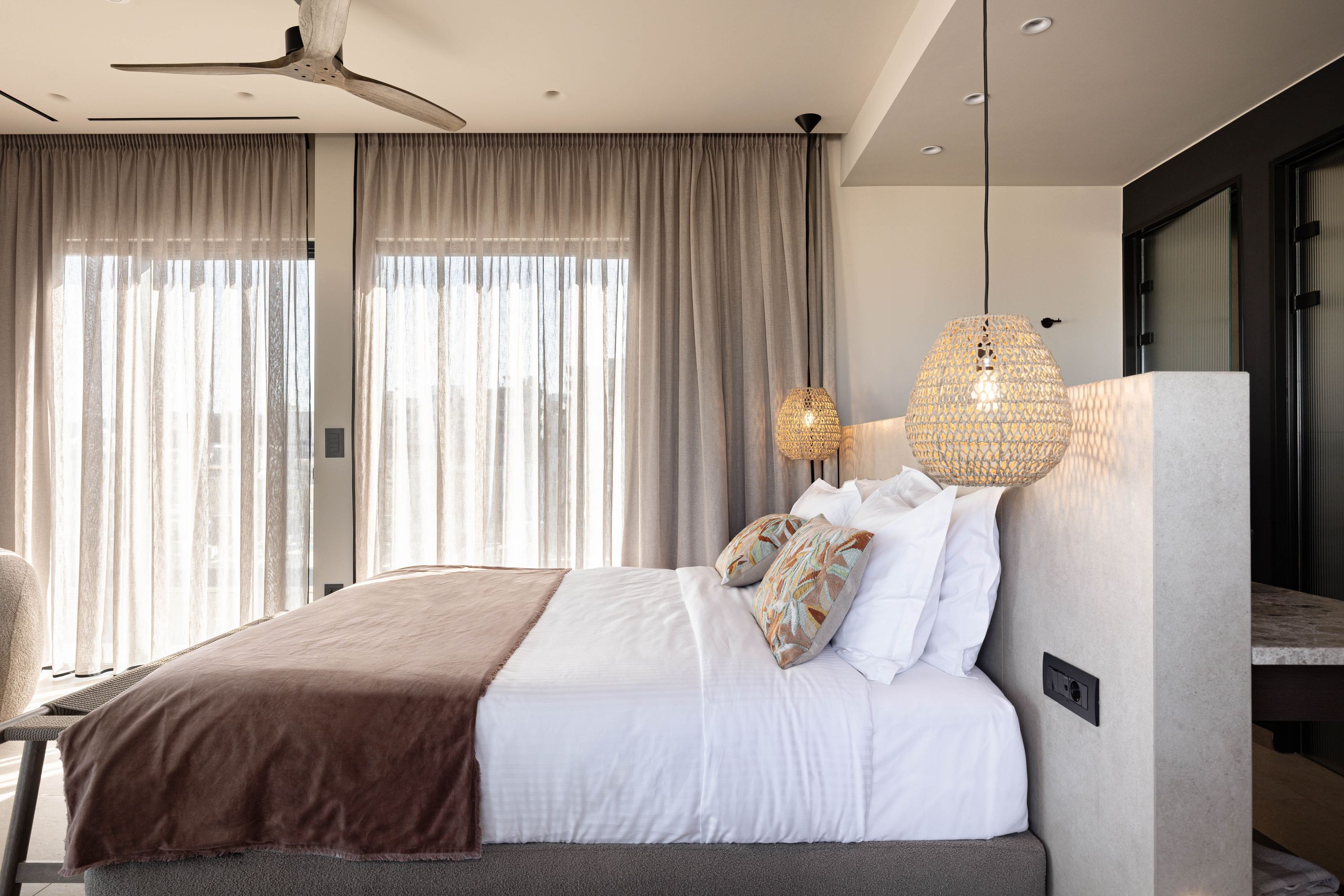 Una moderna camera d'albergo con un letto grande, una ventola a soffitto e un'ampia finestra con tende.