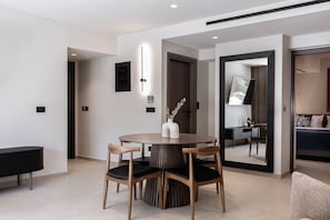 A modern hotel room with a round dining table, wooden chairs, a black console, and a large mirror. - Moncasa Suites (Agios Nikolaos)