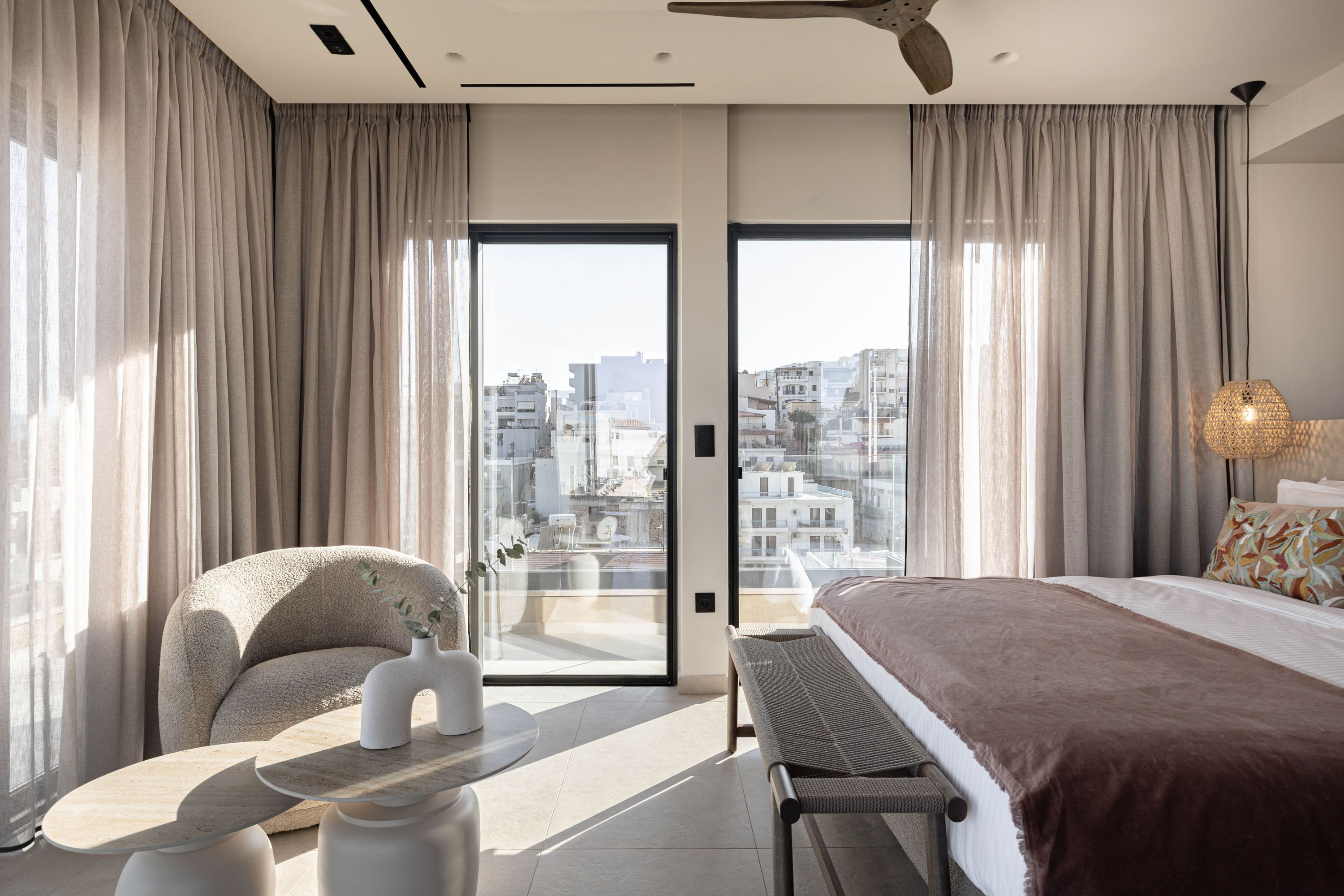 Een moderne hotelkamer met een bed, een zithoek, een tafel en uitzicht op de skyline door grote ramen.