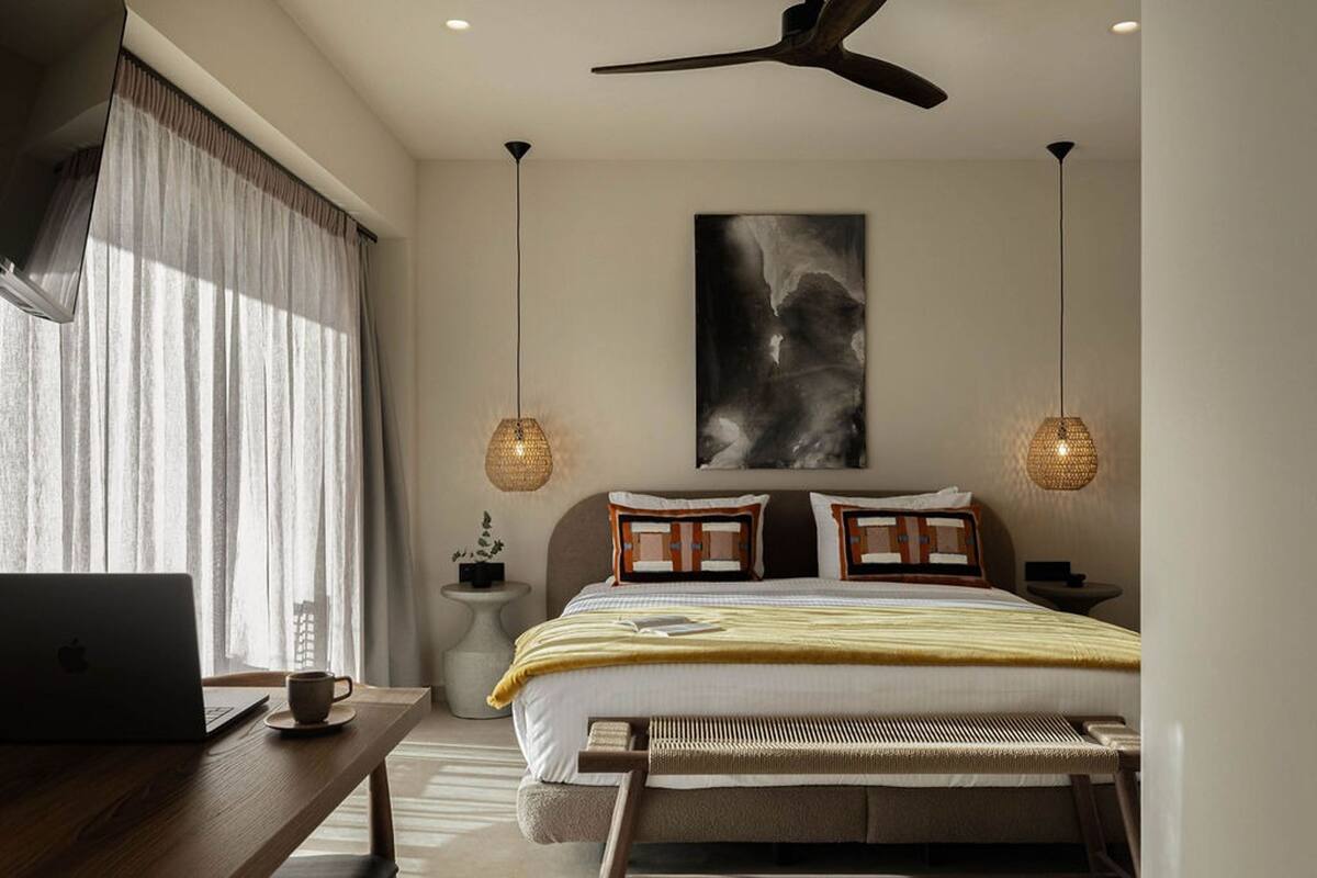A bedroom with a bed, bedside table, lamp, laptop, and a ceiling fan.
