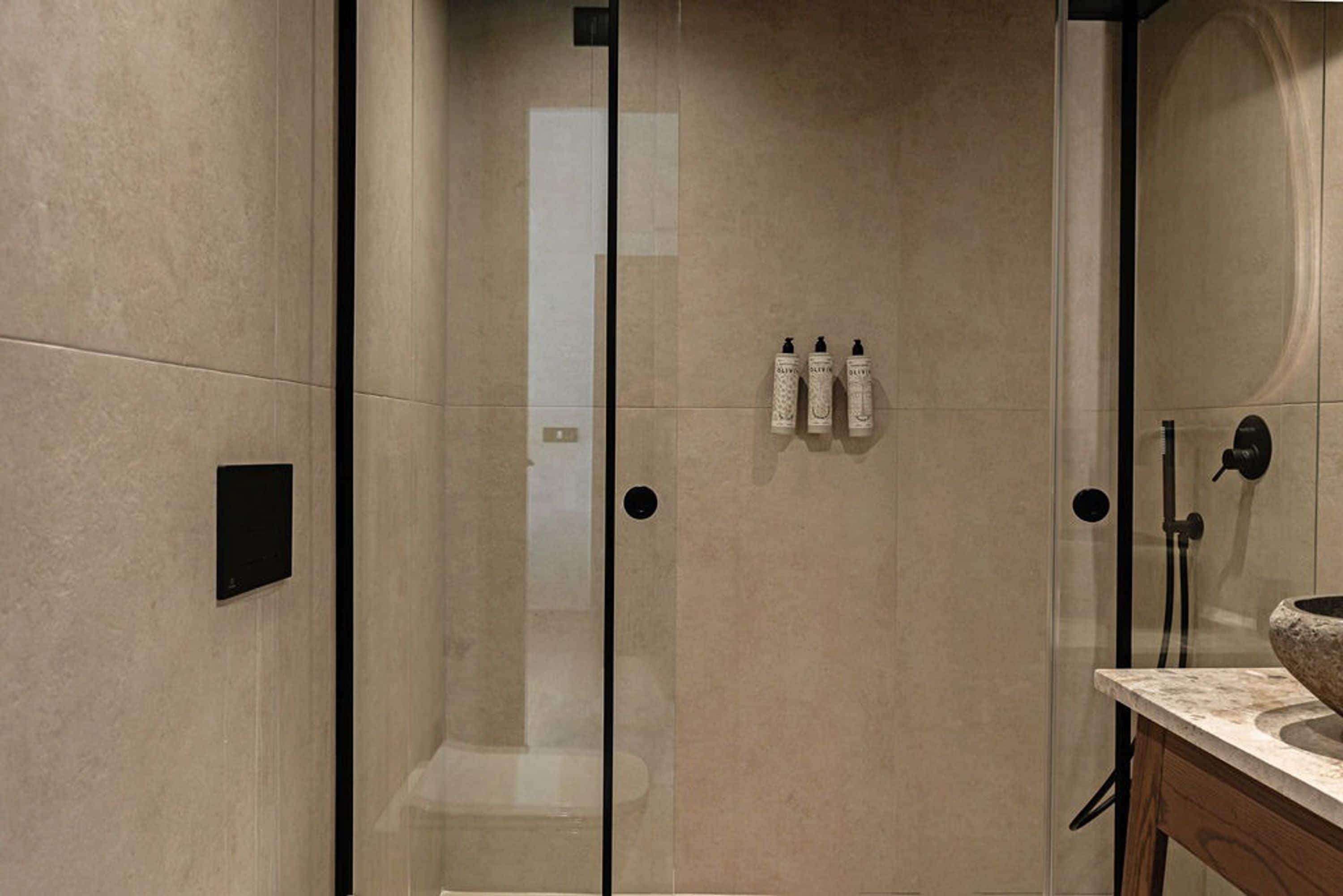 Een moderne badkamer met een douchecabine van glas, een marmeren wastafel en drie toiletartikelen op de muur.