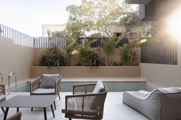 Une terrasse extérieure moderne, dotée de meubles en osier, d’une piscine et d’une végétation luxuriante.