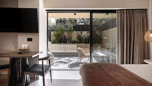 A modern hotel room with a large bed, a dining area, a TV, and a balcony with plants. - Moncasa Suites (Agios Nikolaos)