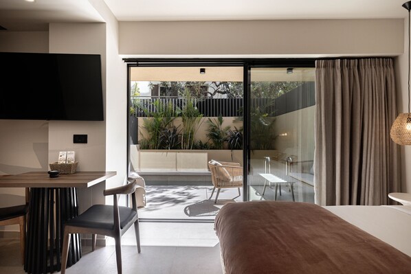 A modern hotel room with a large bed, a dining area, a TV, and a balcony with plants. - Moncasa Suites (Agios Nikolaos)