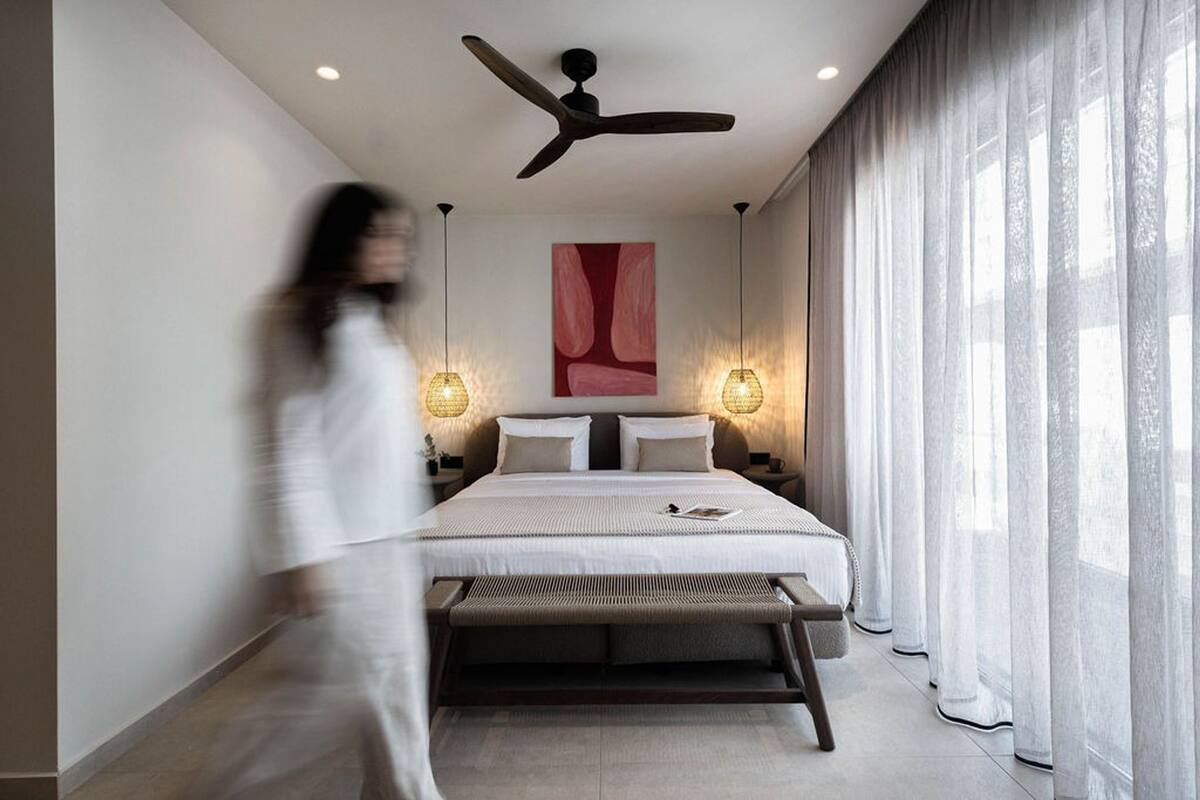 A modern bedroom with a bed, bedside lamps, a ceiling fan, and sheer curtains.