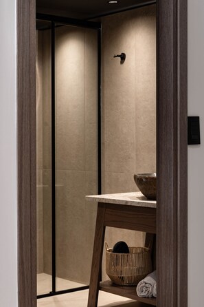 A modern bathroom with a wooden-framed glass door, a stone sink, and a woven basket. - Moncasa Suites (Agios Nikolaos)