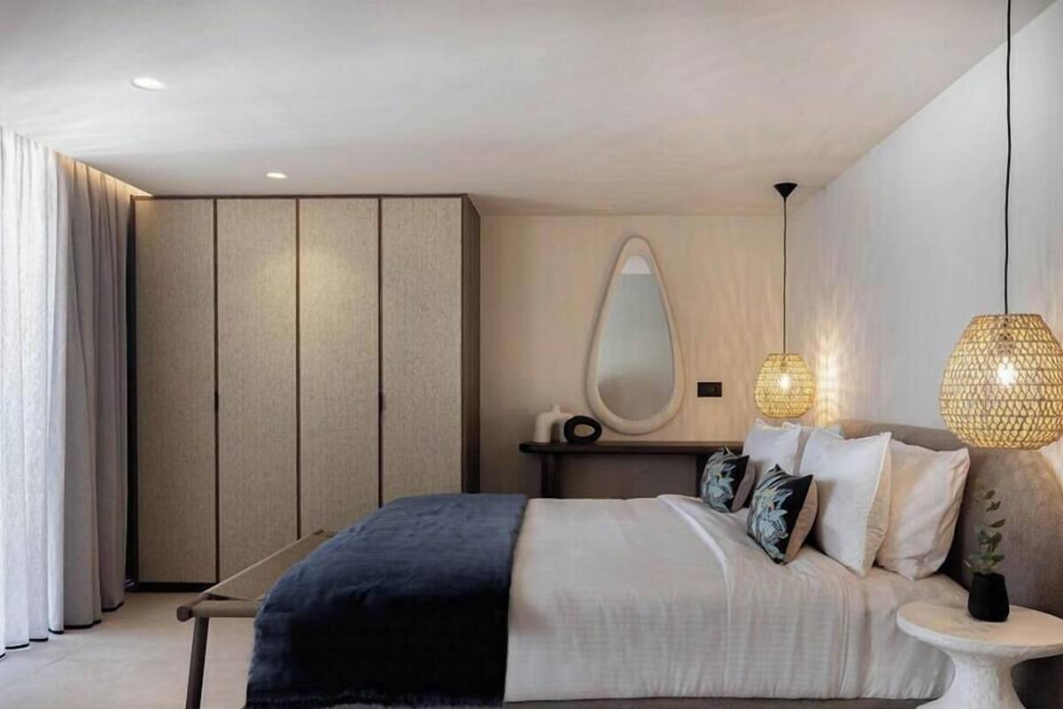 A modern bedroom with a bed, bedside table, mirror, and two wall-mounted lamps.