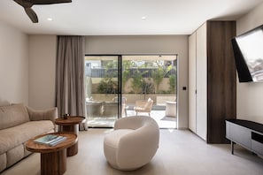 A modern living room with a sofa, a round coffee table, a white armchair, and a TV mounted on the wall. - Moncasa Suites (Agios Nikolaos)
