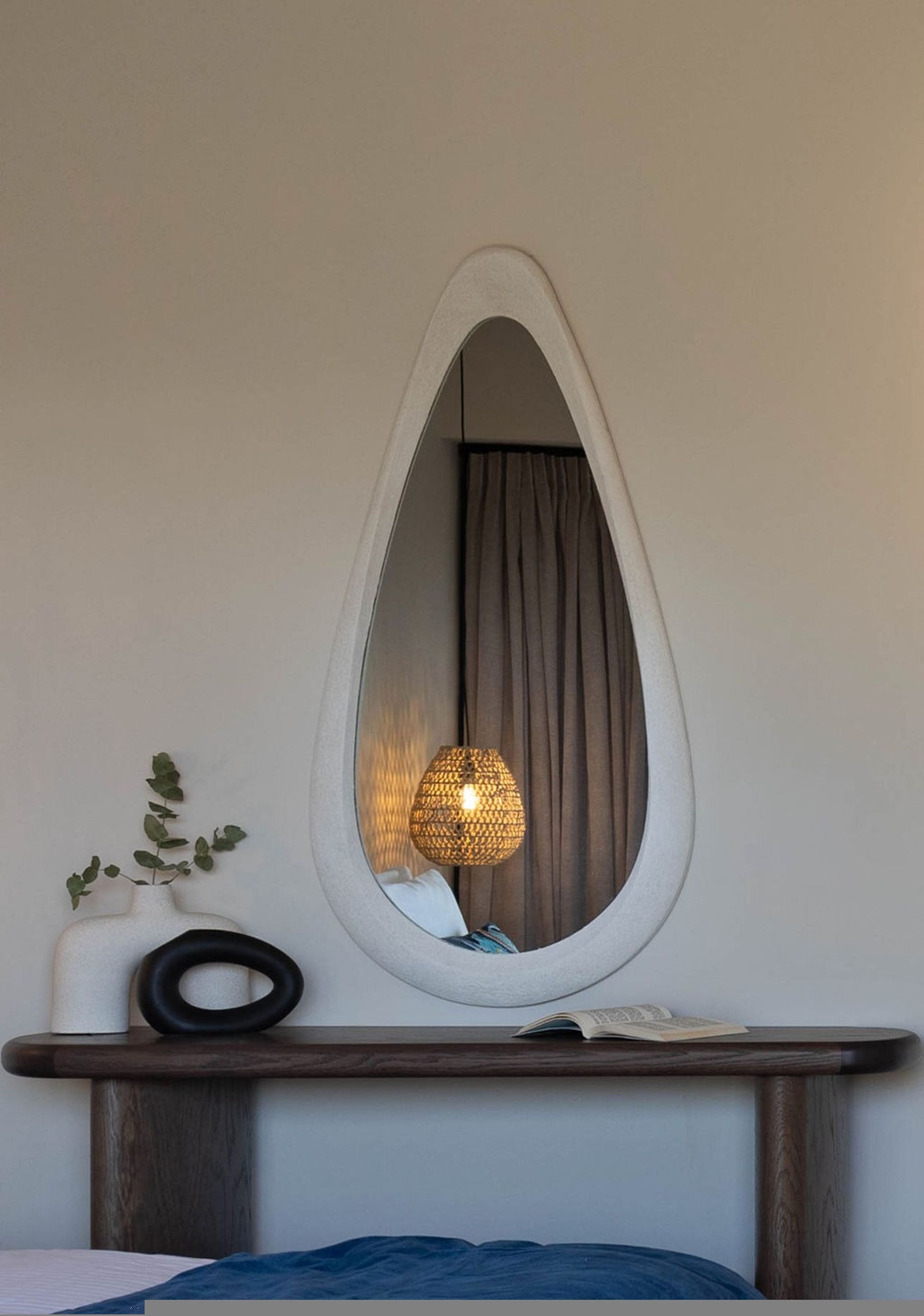 Una habitación con un espejo ovalado grande, una mesita de noche, una lámpara y una planta.