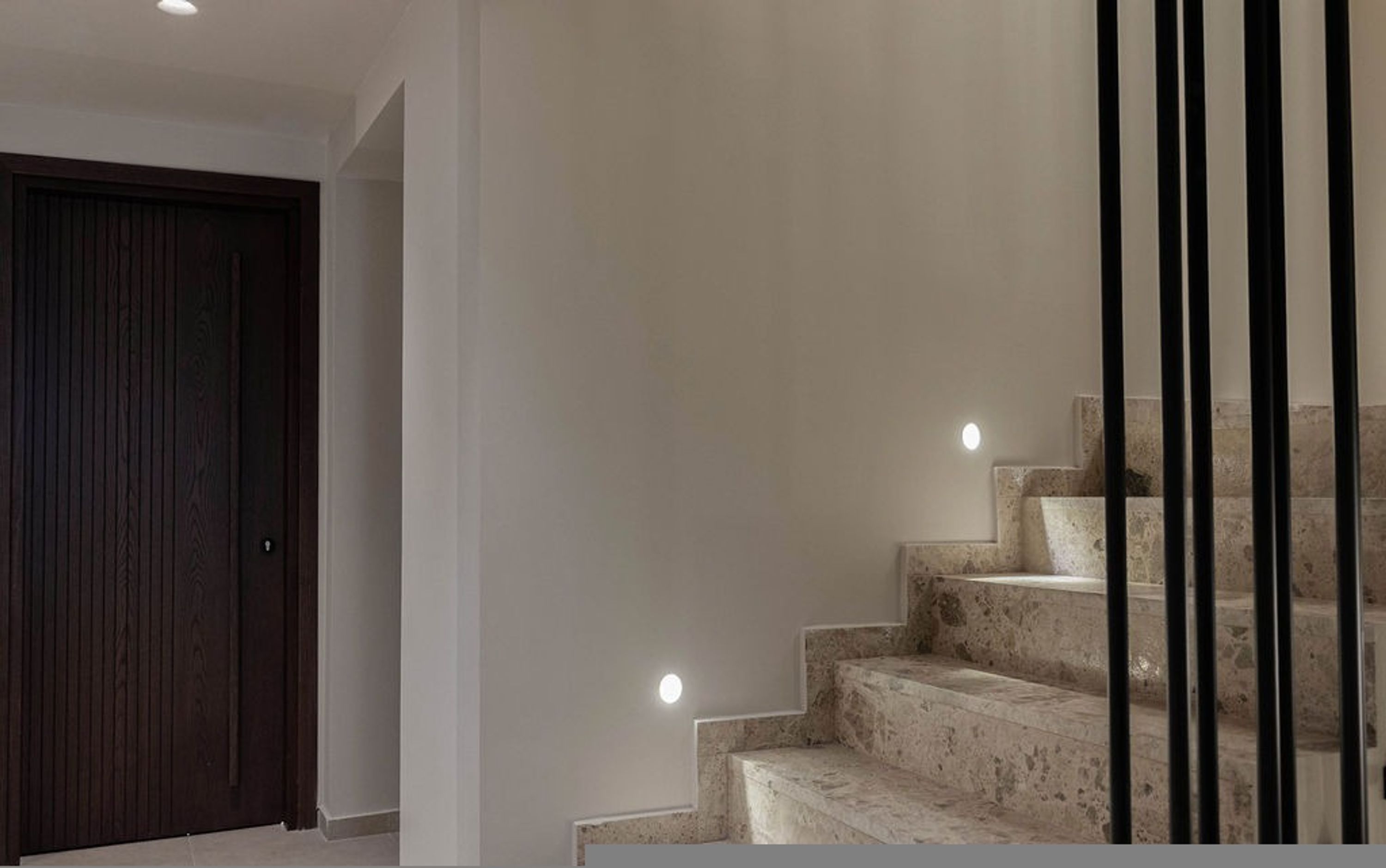 Una escalera con revestimiento de piedra, una puerta de madera oscura e iluminación empotrada.