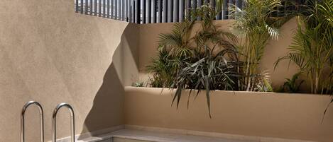 A swimming pool with metal railings, a beige wall, and potted plants.