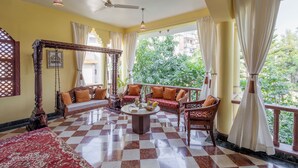 A room with a checkered floor, a canopy bed, a sofa set, a coffee table, and a view of greenery outside. - Alaya Stays 4 BHK with Outdoor Dining Area - Abhimanyu Mansion Sapphire (Udaipur)