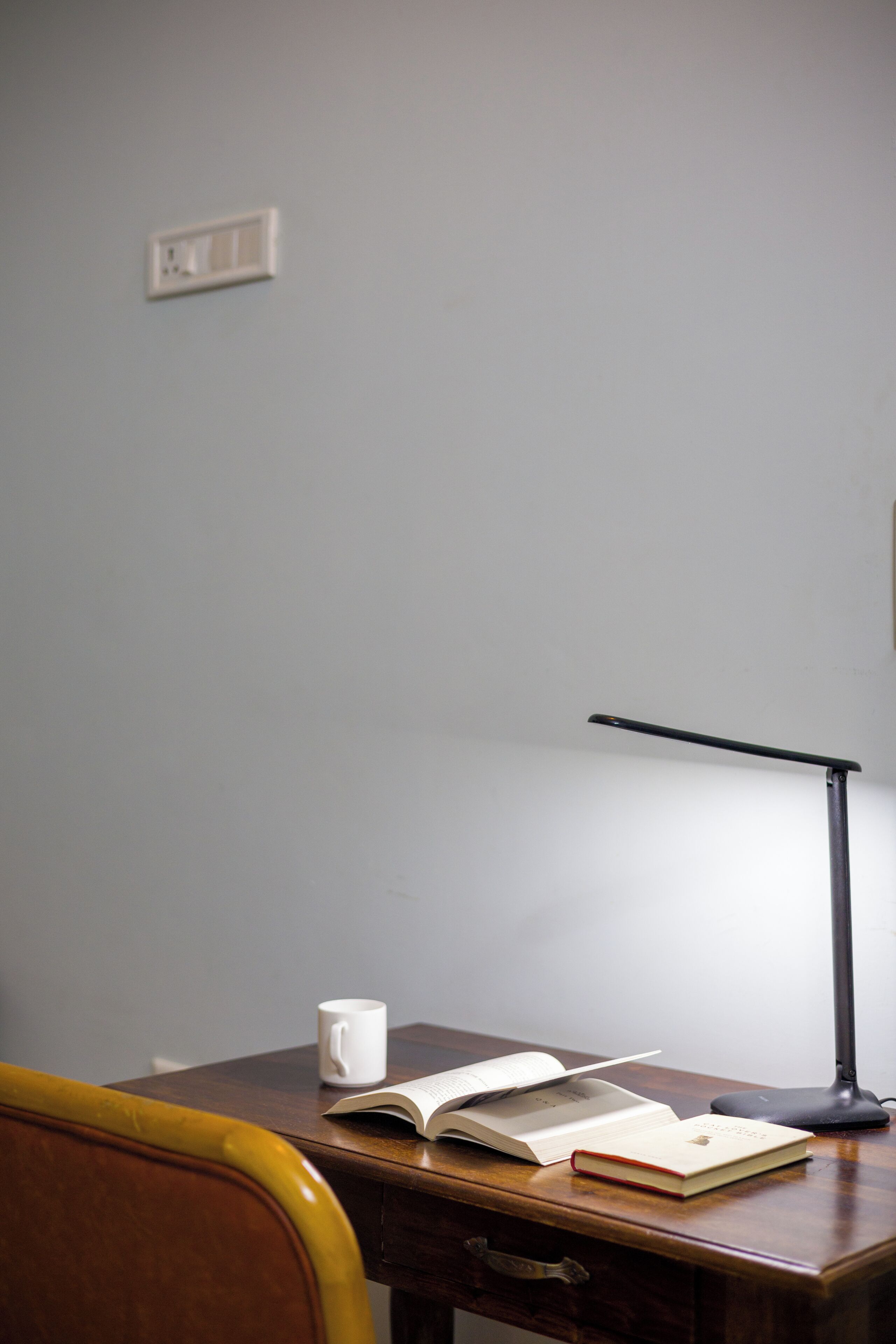 A wooden desk with an open book, a white mug, and a desk lamp.