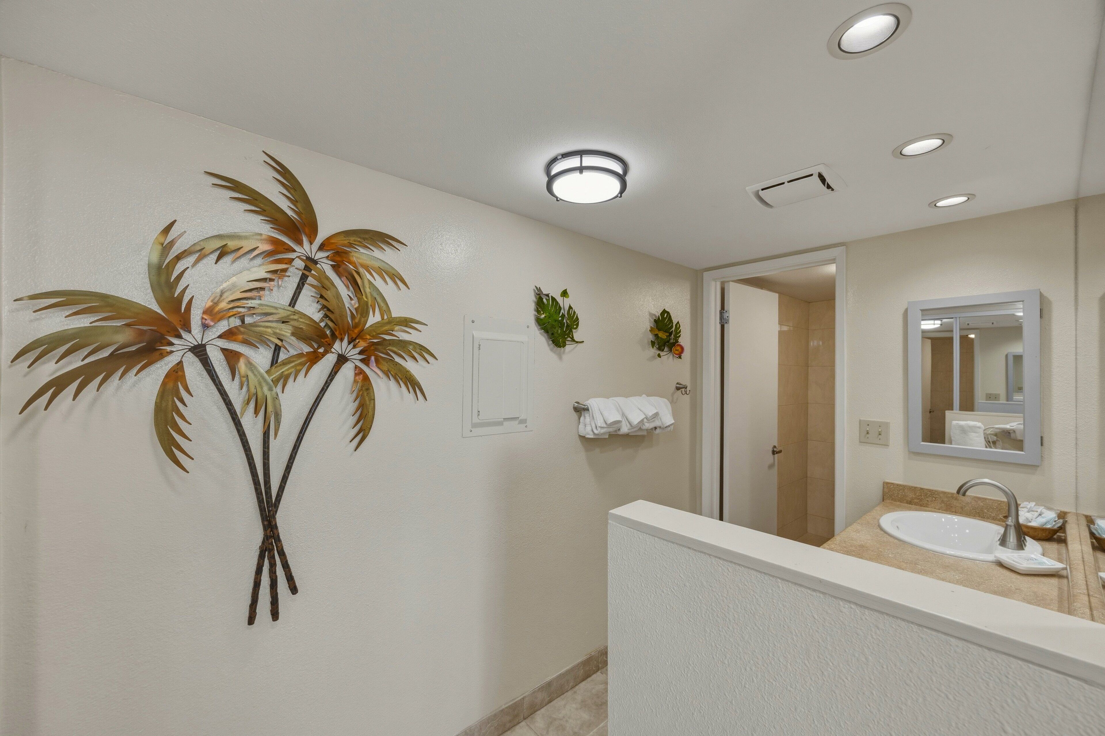 Une salle de bain équipée d’un lavabo, d’un miroir, d’un porte-serviettes et d’une plante décorative.