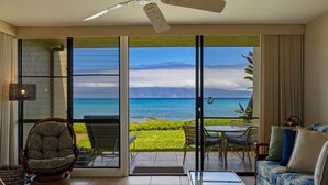 A room with a view of the ocean, a ceiling fan, a wicker chair, a sofa, and a dining area with chairs and a table. - Oceanfront Maui Point Condo Sleeps 4 - Unit A3 1 Bedroom Condo (Lahaina)