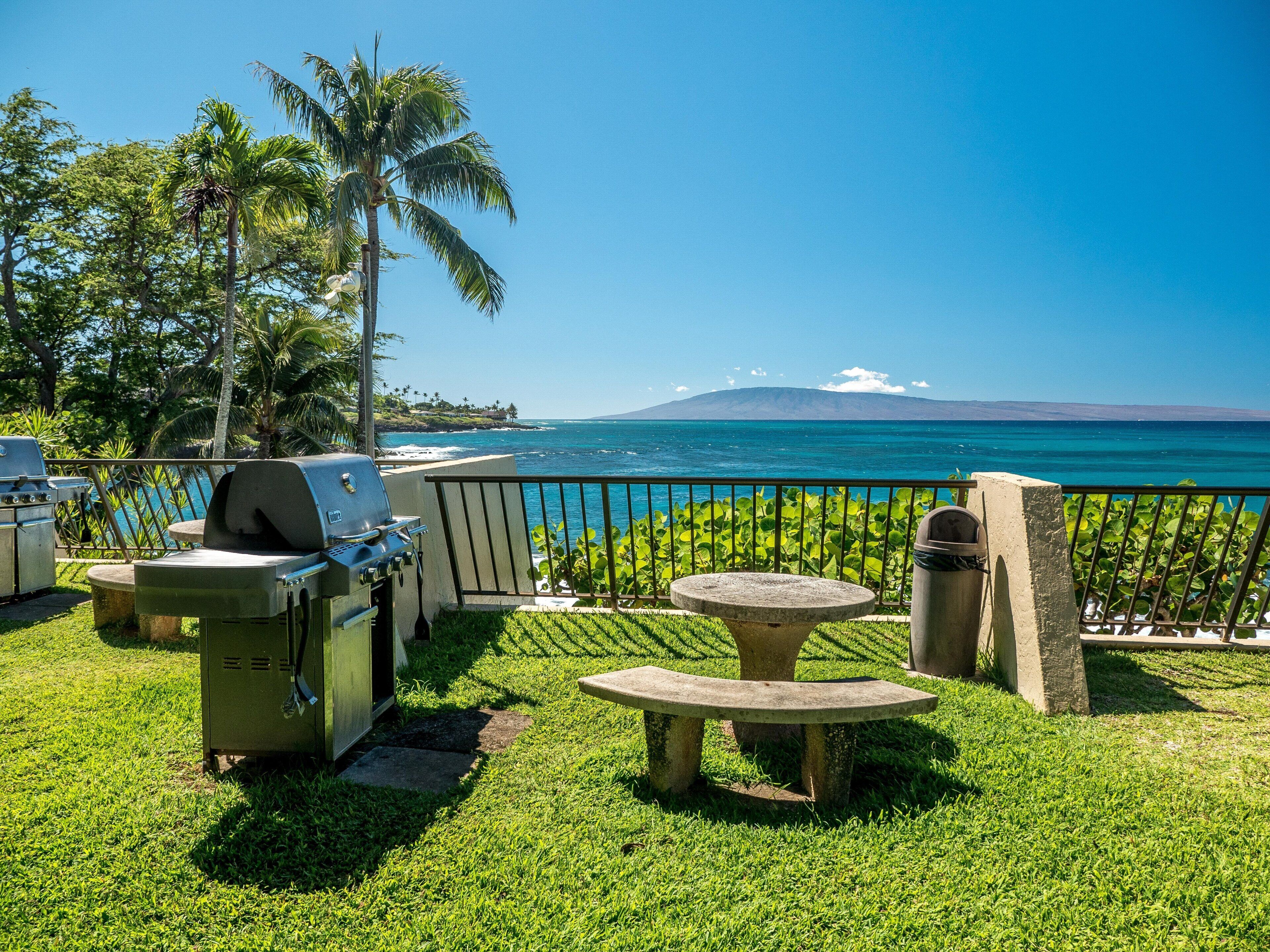 A patio with a grill, seating, and a view of the ocean.