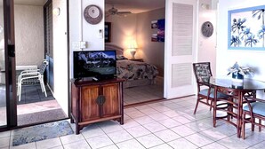 Ein Hotelzimmer mit Bett, Fernseher, Essecke mit Stühlen und Deckenventilator.
