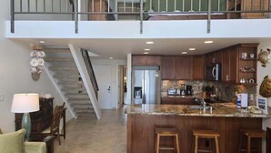 A spacious living area with a kitchen island, a staircase, and a dining area. - Napili Point Oceanfront Family Loft - Unit C4 1 Bedroom Condo (Lahaina)