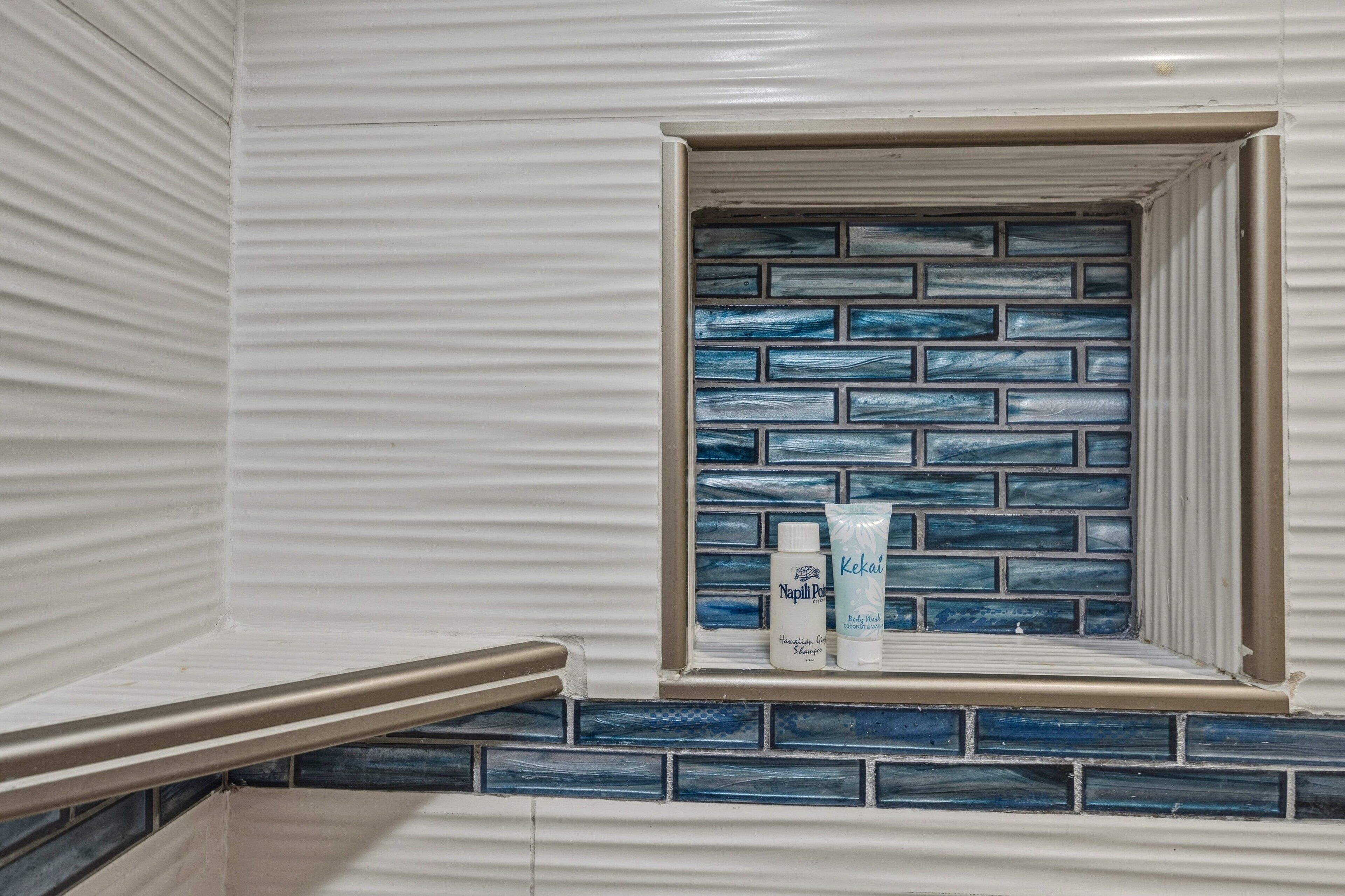 Un baño con pared de azulejos, una ventana con diseño de ladrillo azul y un estante con artículos de aseo.